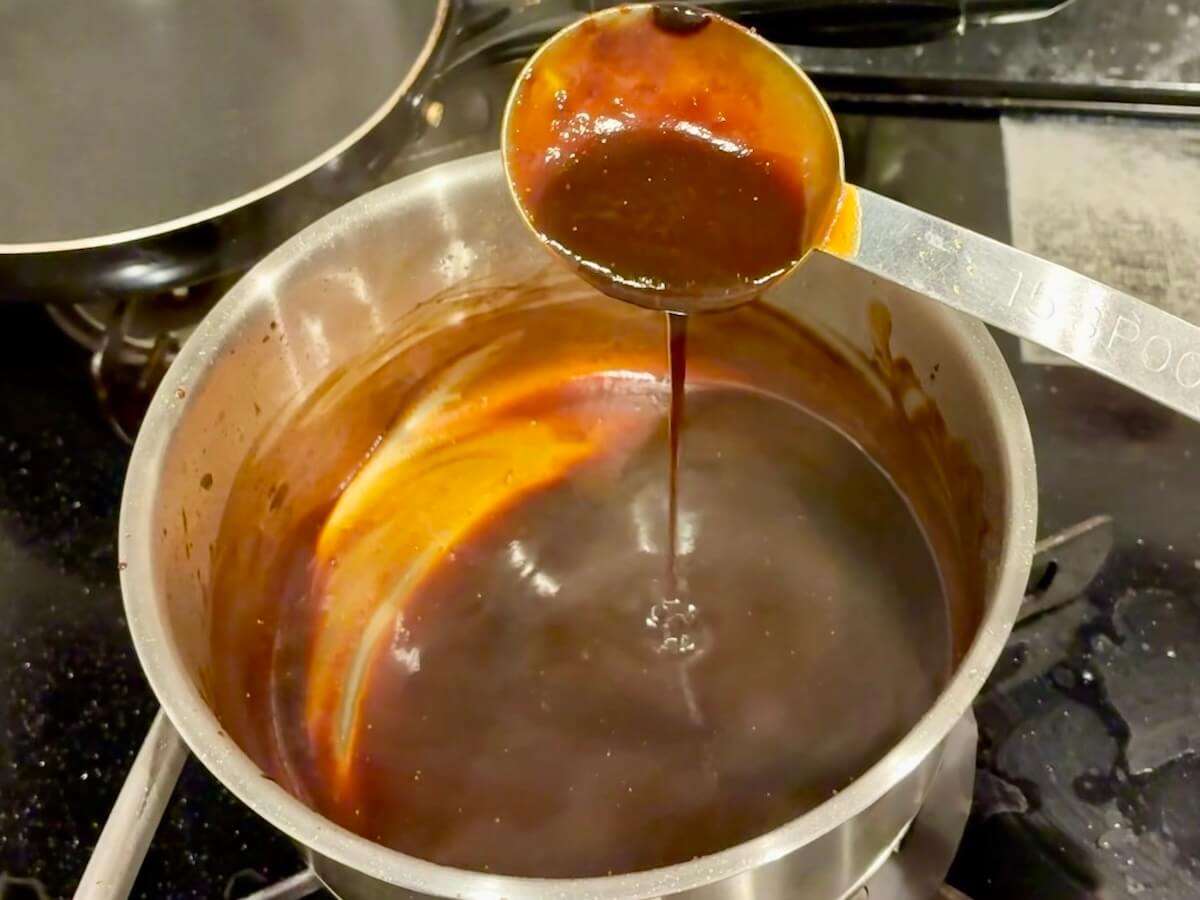 お玉から細く流れ落ちる加熱直後の味噌だれ